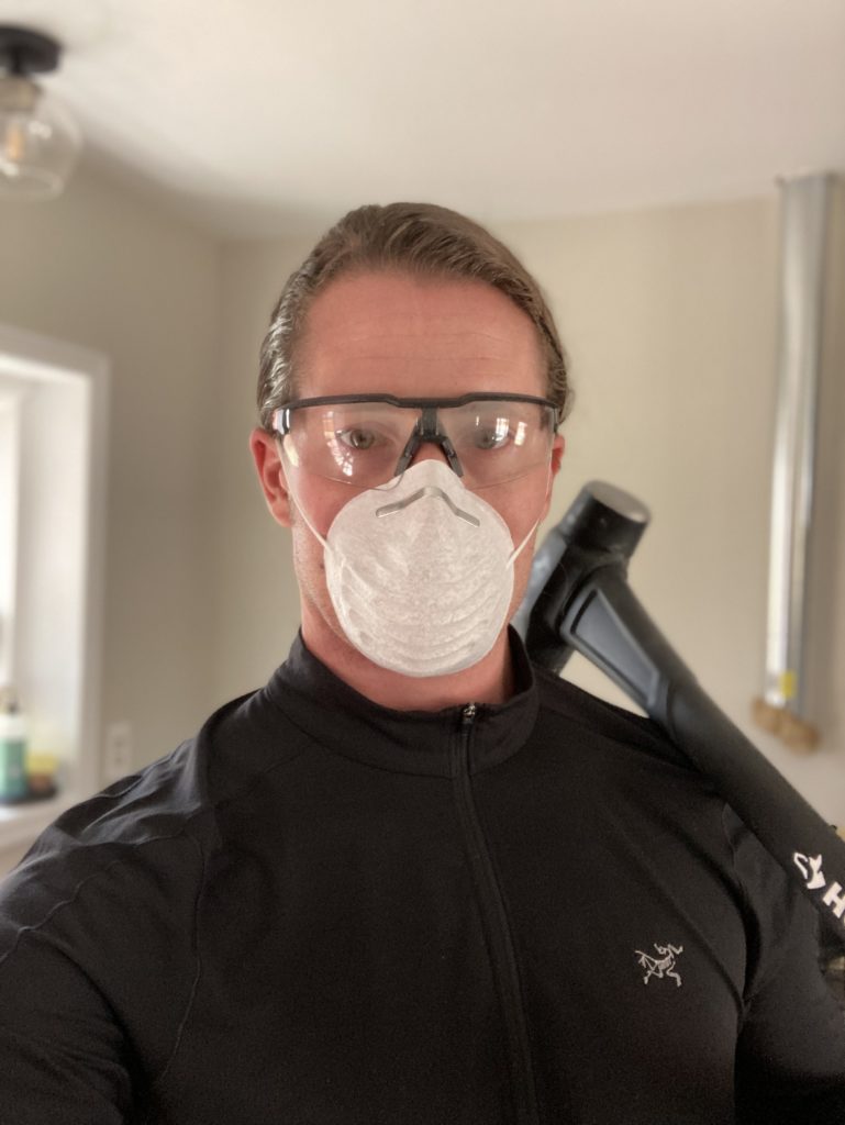 Man wearing safety glasses and mask while holding a hammer.